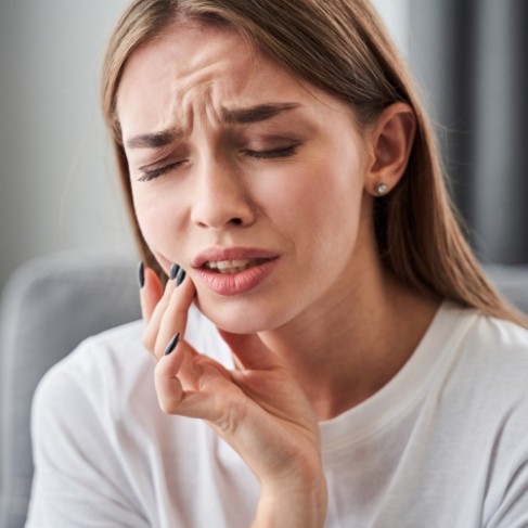 Woman touching her cheek in pain before emergency dentistry in Louisville