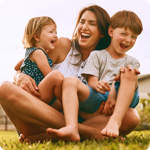 Woman laughing with her two young kids in grass