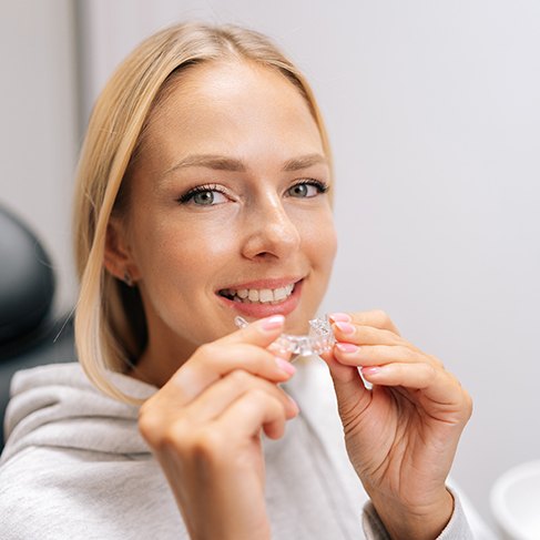 Woman smiling while holding Invisalign aligner